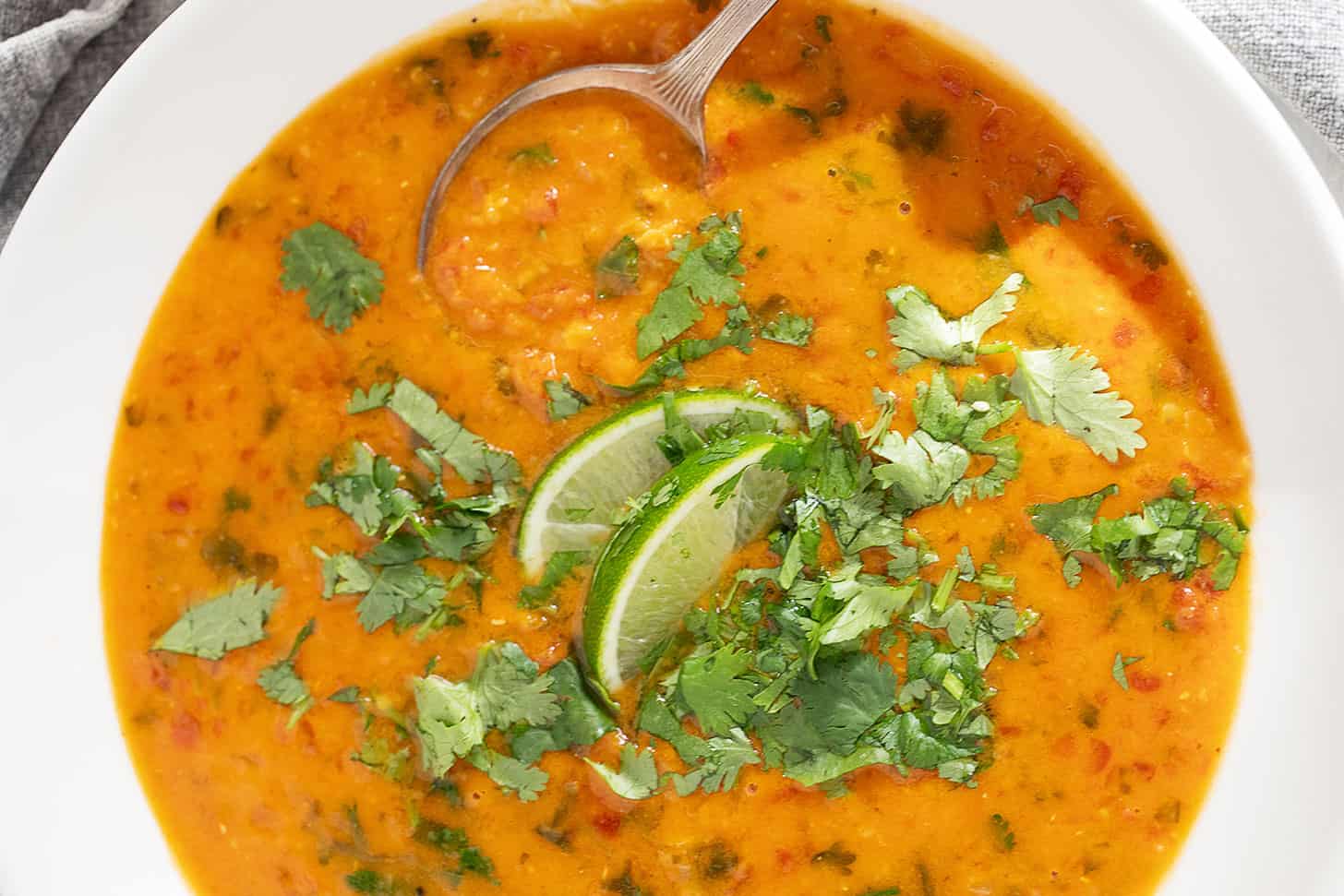 Coconut curry lentil soup in a bowl with cilantro garnish and lime wedges.