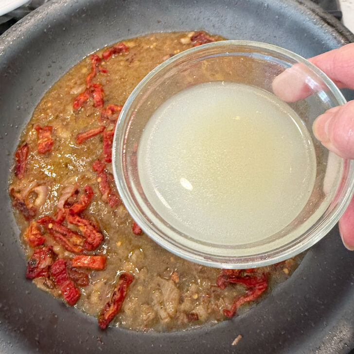 Adding chicken broth to the skillet.