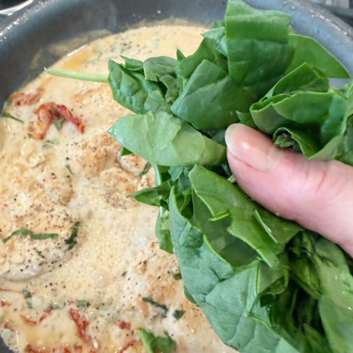 Adding chopped spinach to the skillet for the creamy sun-dried tomato chicken.