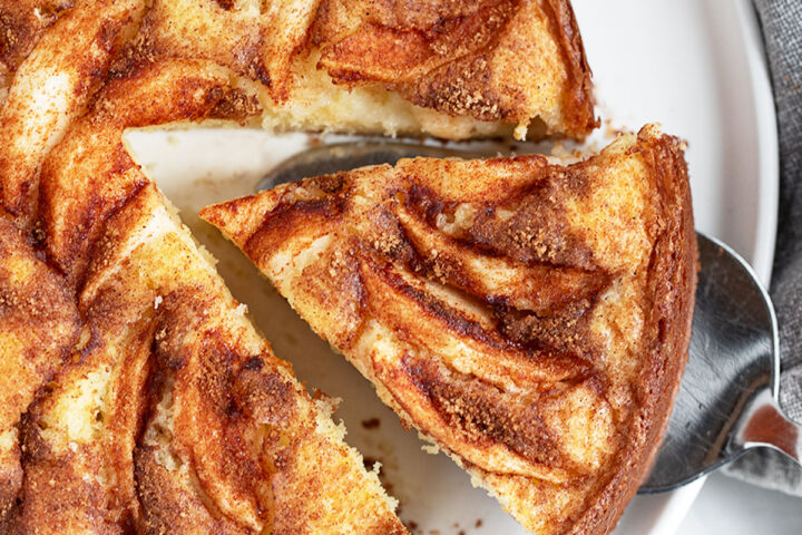 Dutch apple cake on a serving plate with a slice cut out.