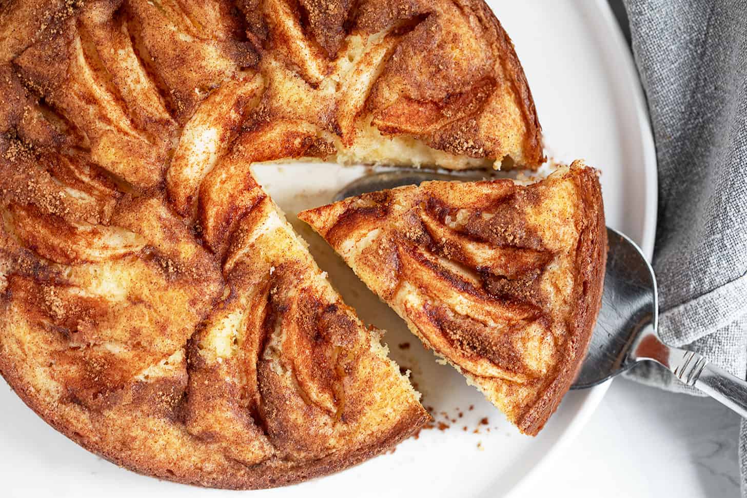 Dutch apple cake on a serving plate with a slice cut out.