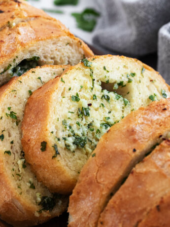 Easy herb and garlic bread loaf made from a whole bread loaf, sliced on a serving board.