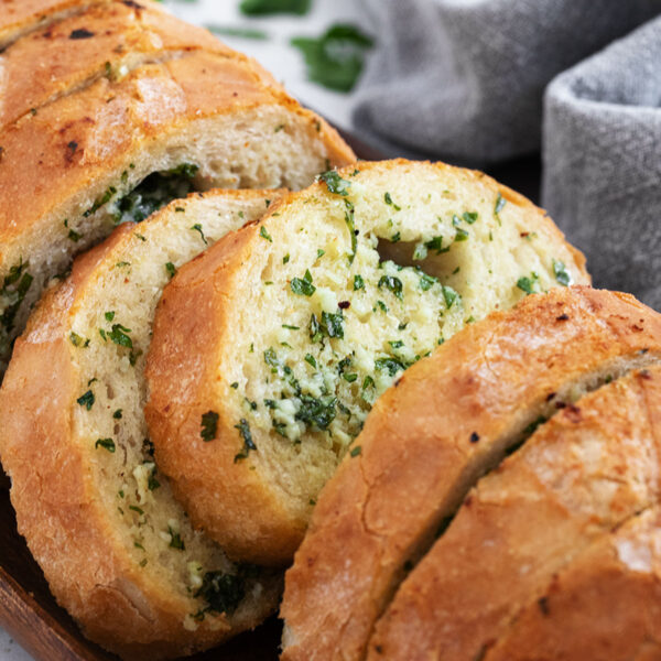 Easy herb and garlic bread loaf made from a whole bread loaf, sliced on a serving board.