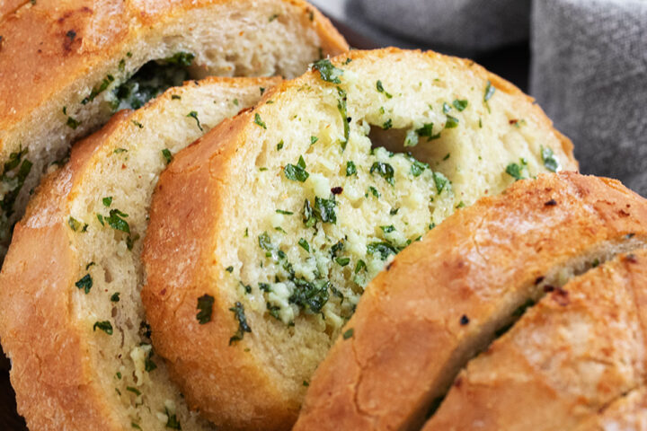 Easy herb and garlic bread loaf made from a whole bread loaf, sliced on a serving board.