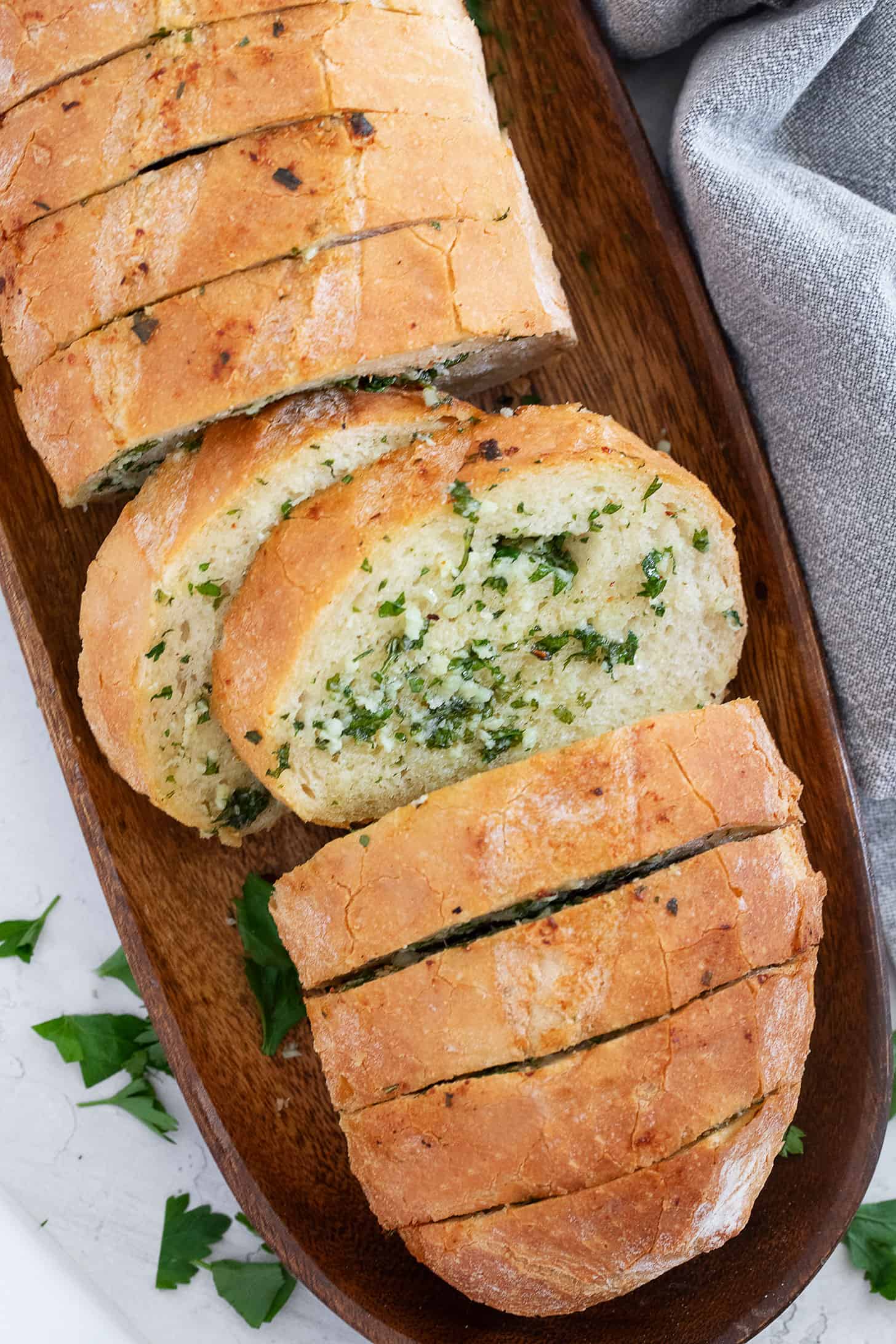 Easy herb and garlic bread loaf made from a whole bread loaf, sliced on a serving board.