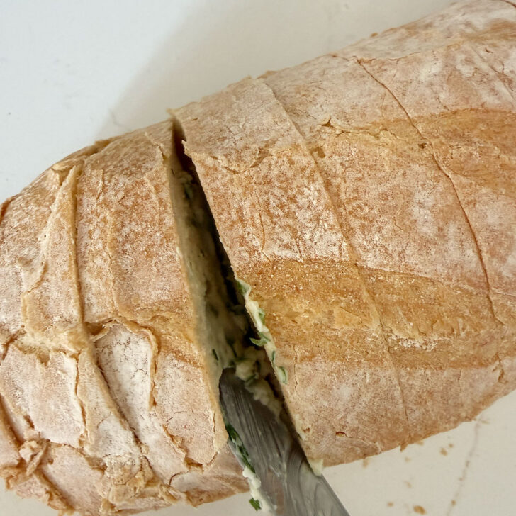 Spreading the herb and garlic butter onto the sliced bread loaf.