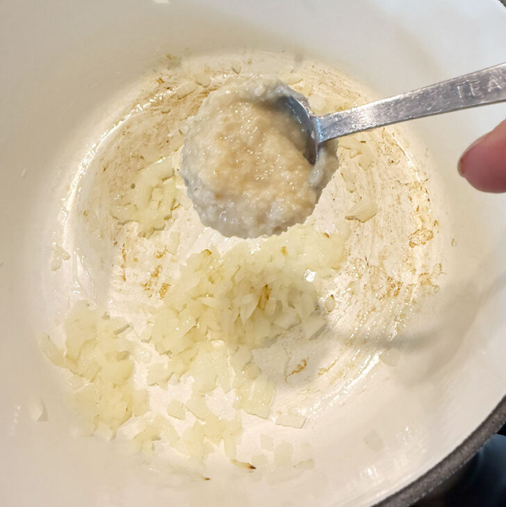 Adding ginger garlic paste to a pot with softened onion.
