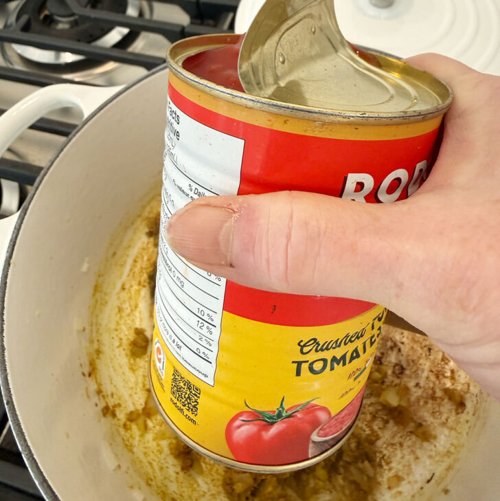 Adding a can of crushed tomatoes to the soup pot.