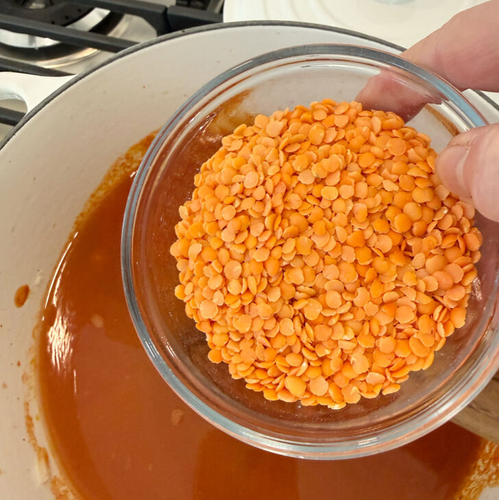 Adding red lentils to the soup pot.