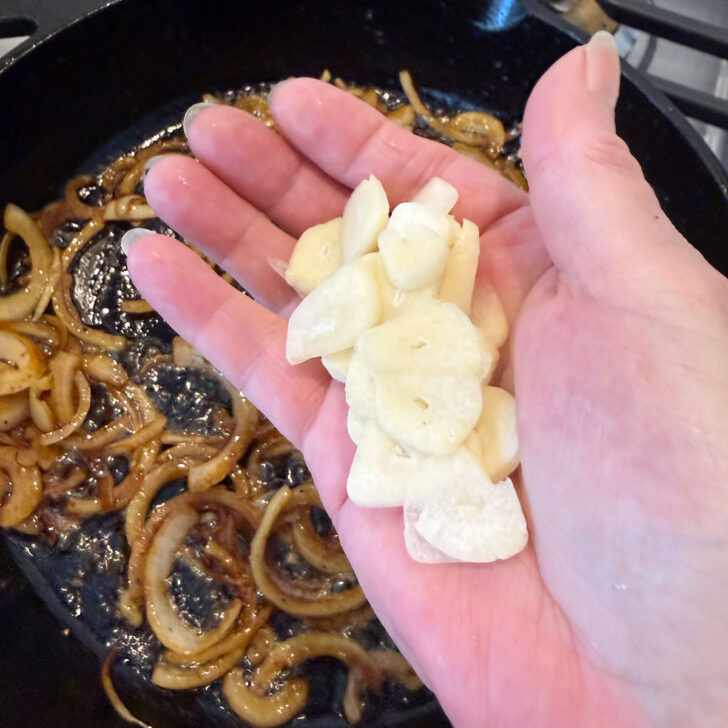 Adding sliced garlic to the skillet with the onions.