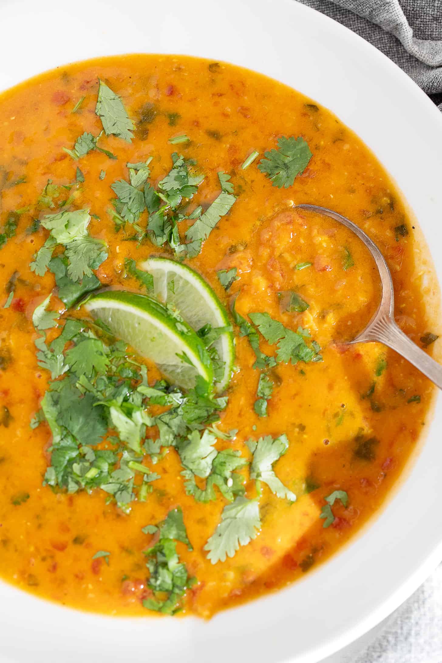 Coconut curry lentil soup in a bowl with cilantro garnish and lime wedges.
